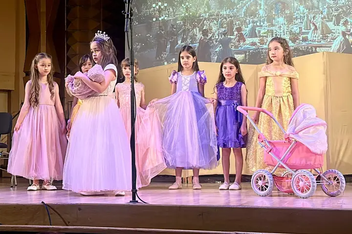 Șase eleve în rochii de prințesă, aliniate pe scenă în fața decorului proiectat