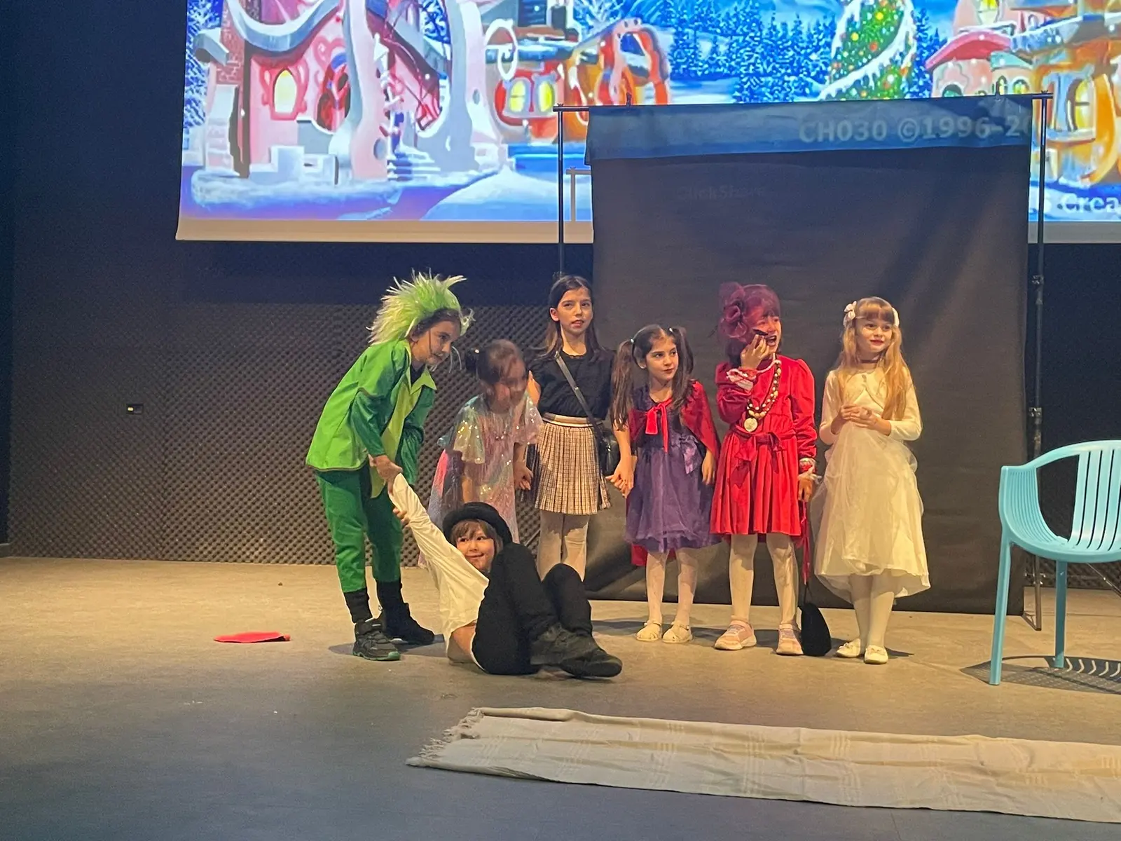 Grup de elevi în costume colorate, pe scenă, în fața unui decor de oraș de poveste