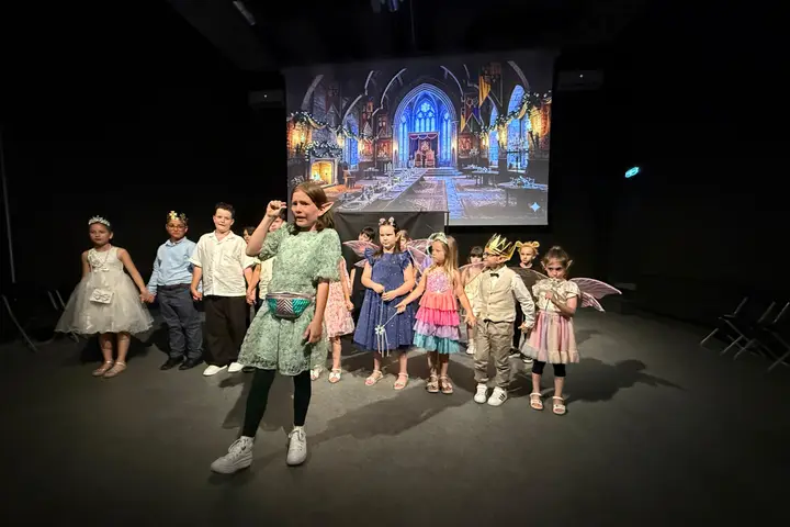 Grup de copii mici în costume de zâne, pe scenă, alături de profesoară